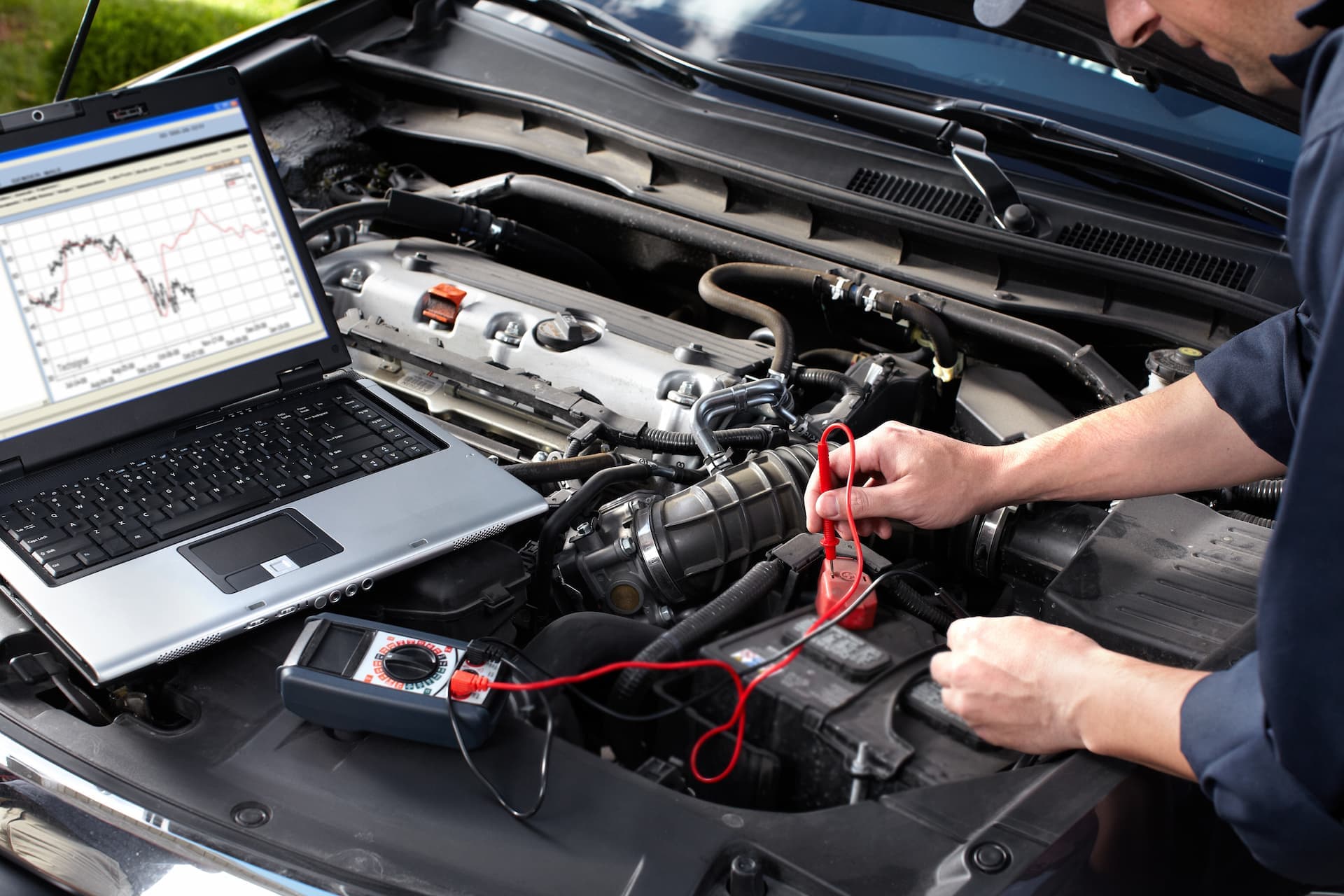 Technician running electronic car diagnostics with a laptop and multimeter